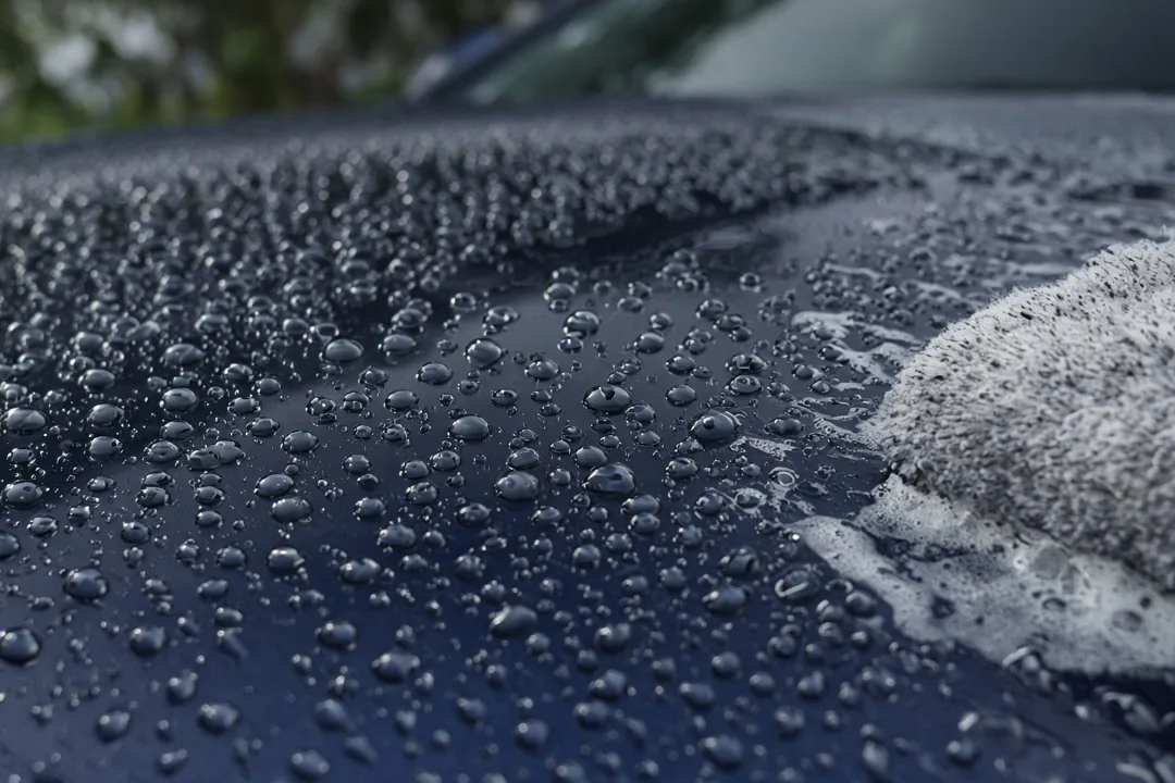 Water beading on the hood of a ceramic coated dark blue car during a gentle hand wash