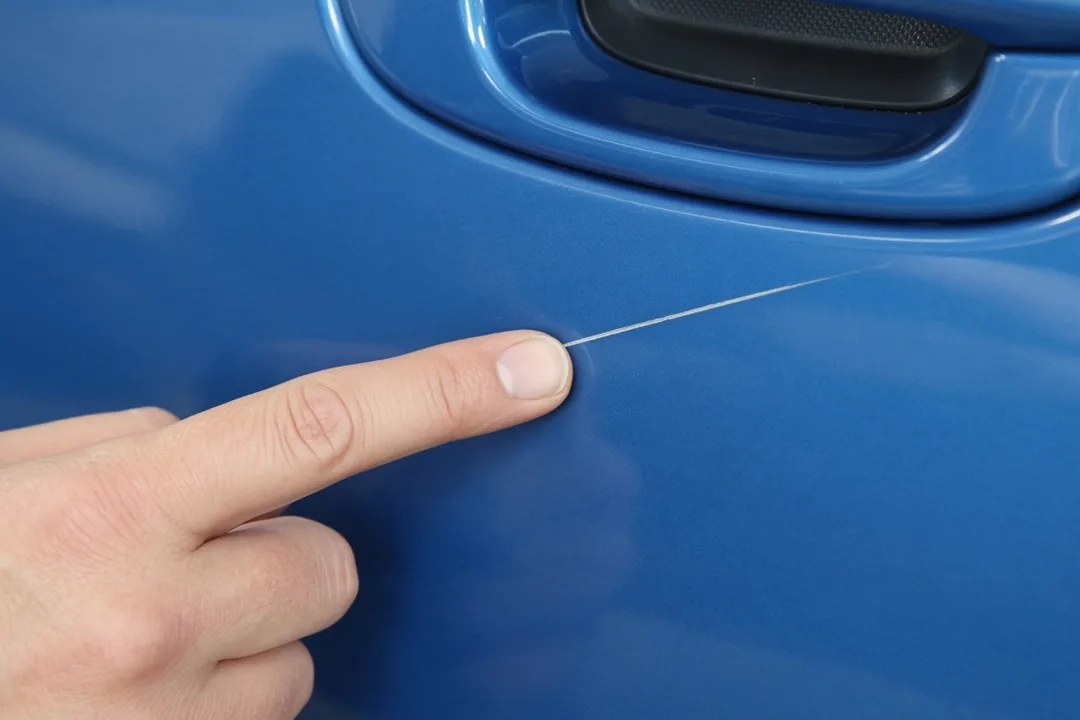 Fingernail test on a light scratch in a blue car door
