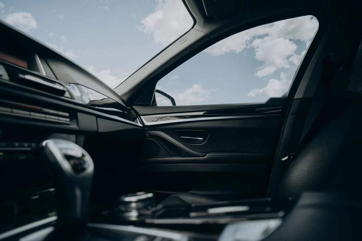 Bright sunlight and blue sky shining through a car's front side window onto a dark interior