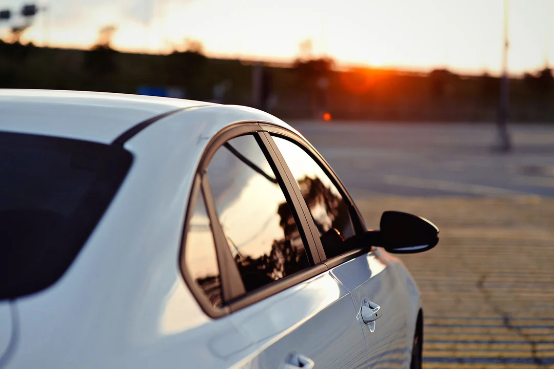 White sedan with light tinted side windows reflecting the evening sun in a parking lot